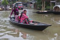 En familj försöker ta sig över en översvämmad väg i byn Burha Burhi i Assam i Indien.