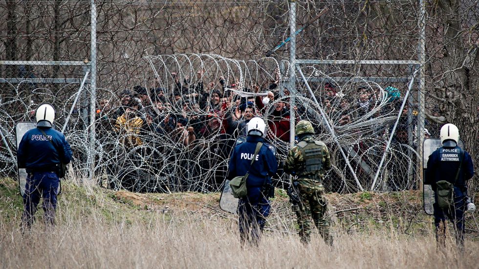Grekisk kravallpolis bevakar migranter vid gränsen till Turkiet. 