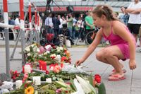 En flicka lägger ner en blomma framför Olympia-köpcentret, där nio unga människor sköts ihjäl på fredagskvällen.
