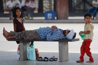 Barn leker vid en sovande man  på en övergiven busshållplats under en storstrejk i Bangalore, Indien. 