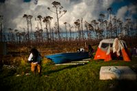Tre män röjer på sina orkanhärjade ägor på ön Grand Bahama, där de slagit upp ett tält för att få sovplats för natten.