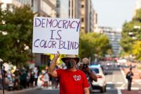 En man håller upp skylten ”Demokratin är färgblind” under en rösträttsdemonstration i Washington DC. Men numera avfärdas ofta tanken om färgblind universalism som naiv.
