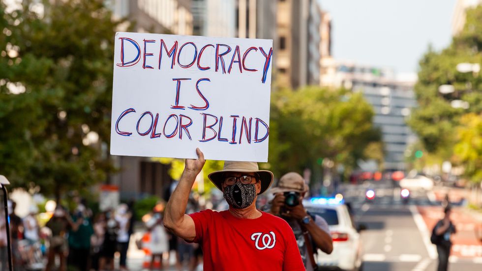 En man håller upp skylten ”Demokratin är färgblind” under en rösträttsdemonstration i Washington DC. Men numera avfärdas ofta tanken om färgblind universalism som naiv.