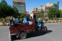 Afghanska kvinnor och barn färdas på en gata i provinshuvudstaden Herat på söndagen medan talibanerna rycker fram mot staden under strider med den afghanska armén.